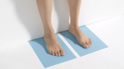Place the sheets of paper on the floor. Stand straight on the paper with your heels against the wall.